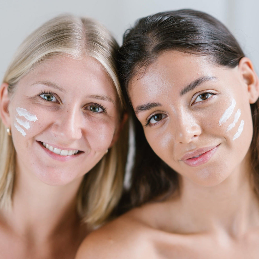 Twee vrouwen glimlachen met witte crème op hun gezichten - Hydraterende Dagcrème met Hyaluronzuur